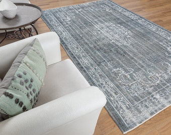 May include: A white armchair with a light green throw pillow sits on a wooden floor with a gray and white patterned rug. The rug has a floral design and a distressed look.