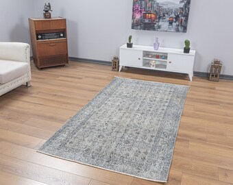 May include: A light gray area rug with a vintage floral pattern. The rug is on a hardwood floor in a room with a white entertainment center and a white couch.