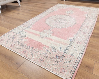 May include: A pink and cream vintage rug with a floral pattern and a central medallion. The rug has a distressed look and is perfect for adding a touch of bohemian style to your home.