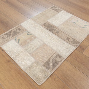May include: A rectangular, patchwork rug with a neutral color palette. The rug features various rectangular and square patches in shades of beige, cream, and light brown. Some patches have subtle geometric patterns. The rug is placed on a wooden floor.