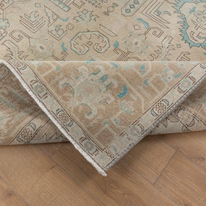 May include: A close-up of the edge of a beige rug with a blue and white geometric pattern. The rug is folded over and the underside is visible.