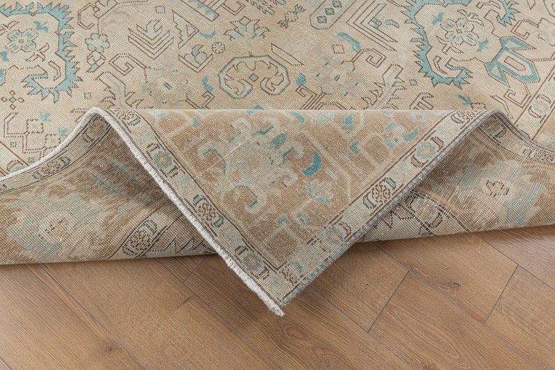 May include: A close-up of the edge of a beige rug with a blue and white geometric pattern. The rug is folded over and the underside is visible.