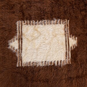 Op de afbeelding: Een bruin en wit koeienhuidkleed met een vierkant stuk wit bont in het midden. Het witte stuk is omgeven door een bruine rand.