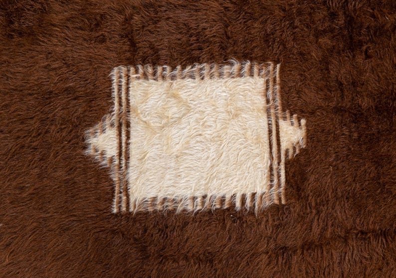 Op de afbeelding: Een bruin en wit koeienhuidkleed met een vierkant stuk wit bont in het midden. Het witte stuk is omgeven door een bruine rand.