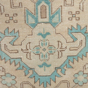 May include: A close-up of a beige rug with a blue and brown geometric pattern. The rug has a traditional design with intricate details.