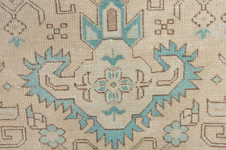 May include: A close-up of a beige rug with a blue and brown geometric pattern. The rug has a traditional design with intricate details.