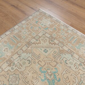 May include: A vintage rug with a beige background and a light blue geometric pattern. The rug has a fringe border.