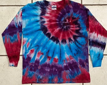 May include: A long-sleeved tie-dye shirt in a spiral pattern. The shirt features a vibrant color scheme of blue, red, and purple. The sleeves and cuffs are solid colors, while the body of the shirt showcases the tie-dye design. The shirt is made of a soft material.