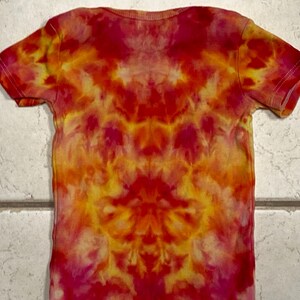 May include: A short-sleeved t-shirt with a tie-dye pattern in shades of red, orange, and yellow. The shirt has a crew neck and a symmetrical design. The fabric appears to be soft and lightweight, suitable for casual wear.