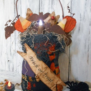 Op de afbeelding: Een Halloween-thema stoffen tas met een zwart en oranje patchwork ontwerp. De tas is versierd met een bord met de tekst "Trick or Treat", een kleine bel en een spin. De tas is gevuld met stoffen spoken, vleermuizen en maïs.