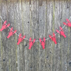 Peut inclure: Une guirlande de homards en papier rouge avec une ficelle blanche suspendue &agrave; une cl&ocirc;ture en bois. La guirlande est faite de homards en papier rouge avec une ficelle blanche.