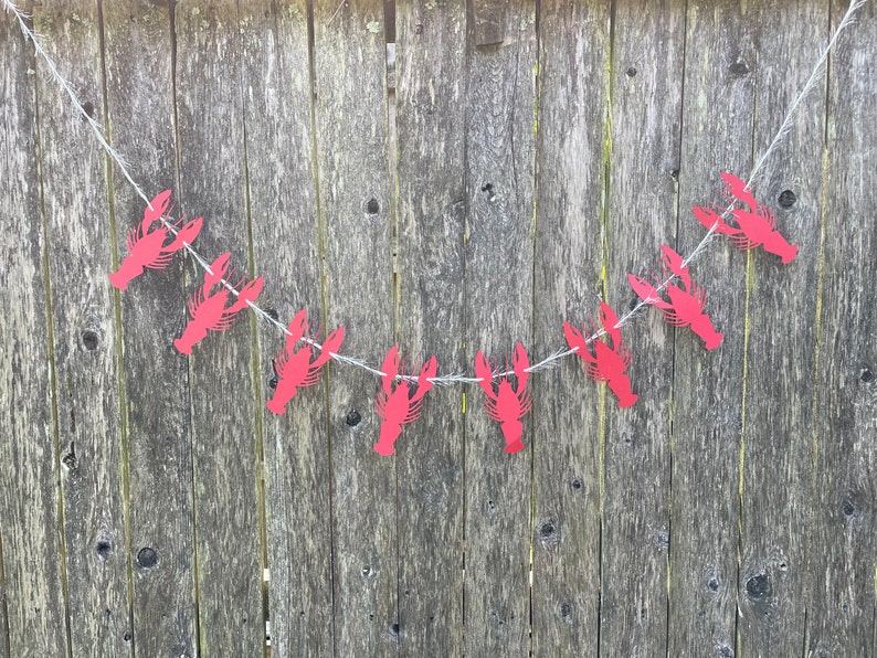 Peut inclure: Une guirlande de homards en papier rouge avec une ficelle blanche suspendue &agrave; une cl&ocirc;ture en bois. La guirlande est faite de homards en papier rouge avec une ficelle blanche.