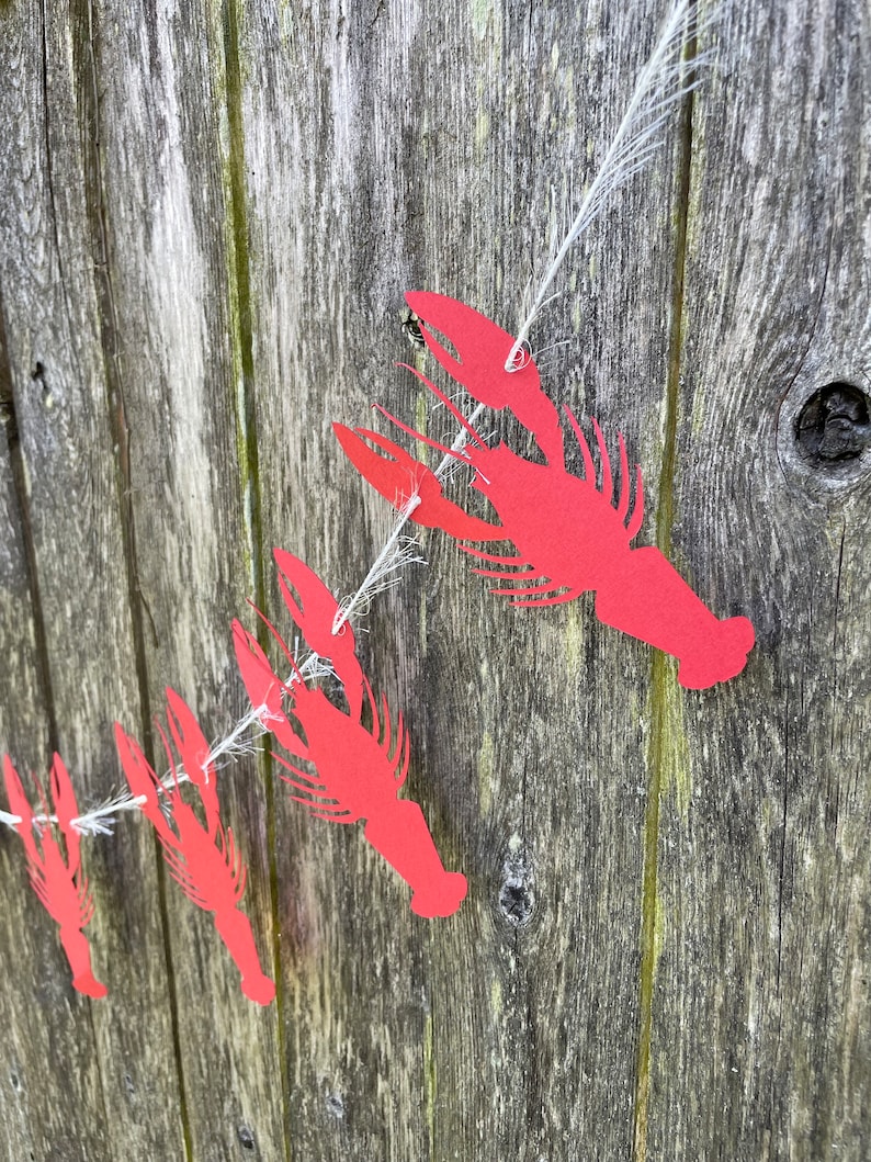 Peut inclure: Une guirlande de homards en papier rouge avec une ficelle blanche suspendue &agrave; une surface en bois.