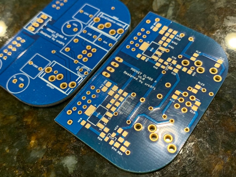 May include: Two blue circuit boards with gold-colored solder points. The top board has the text "POCKET CLASS A" and "Designed by xrk571".