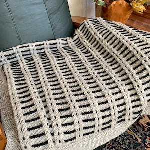 May include: A black and white striped knitted throw blanket with a textured pattern. The blanket is draped over a green leather armchair.
