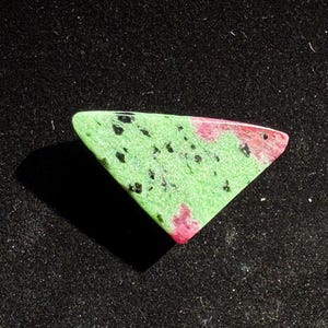May include: A triangular green and pink gemstone with black flecks.
