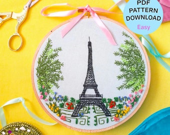 Könnte beinhalten: Stickerei-Hoop-Kunst mit dem Eiffelturm in schwarzem Faden, umgeben von grünem Laub und bunten Blumen. Der Hoop befindet sich auf einem gelben Hintergrund mit rosa und blauen Bändern. Der Text "PDF PATTERN DOWNLOAD Easy" befindet sich in einem weißen Kreis mit rosa Rand.