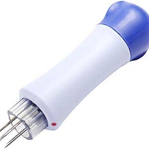 May include: A white and blue handheld tool with multiple needles protruding from one end. The tool has a rounded blue cap and a white body. The needle end is encased in a clear plastic cylinder. A small red dot is visible on the side.