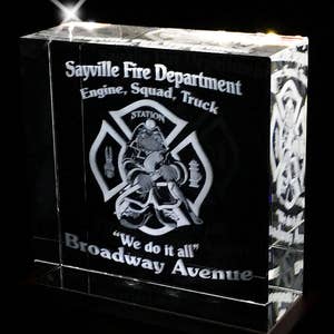 May include: A crystal paperweight with an engraved image of a firefighter in a helmet and a fire hose. The text "Sayville Fire Department Engine, Squad, Truck" is engraved above the image. The text "STATION" is engraved on the firefighter's helmet. The text "We do it all" is engraved below the image. The text "Broadway Avenue" is engraved below the text "We do it all".