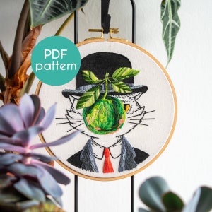 May include: Embroidered hoop art depicting a cat in a bowler hat, suit, and red tie, with a green apple replacing its face. The design includes the text "PDF pattern" in a teal circle. The artwork is set against a white background.