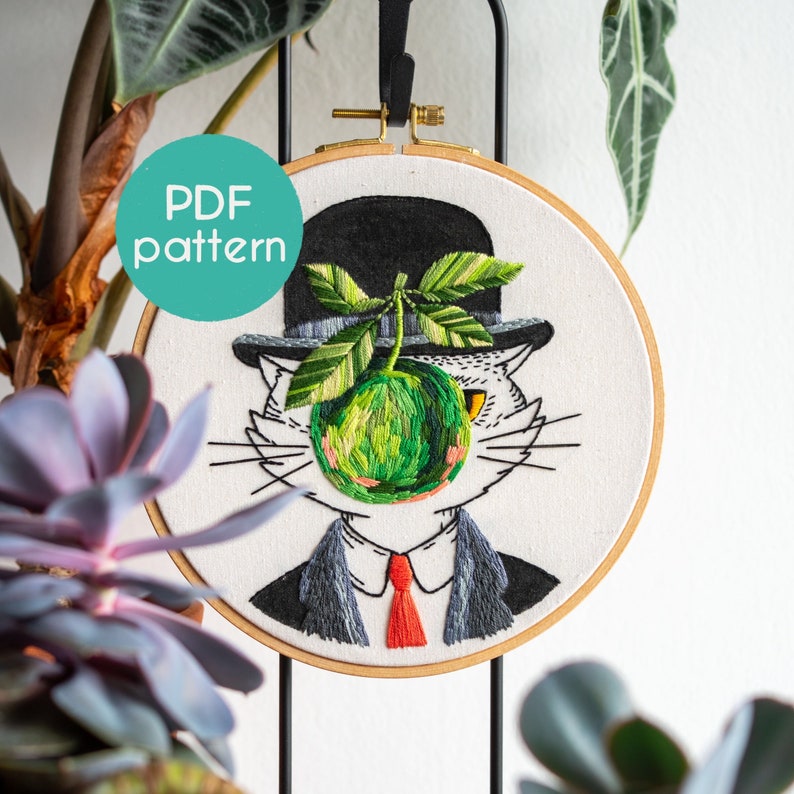 May include: Embroidered hoop art depicting a cat in a bowler hat, suit, and red tie, with a green apple replacing its face. The design includes the text "PDF pattern" in a teal circle. The artwork is set against a white background.