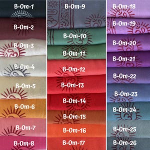 May include: A collection of folded fabric samples in various colors, including teal, burgundy, and orange. Each sample features a sun and Om symbol print in a contrasting color. The samples are labeled with alphanumeric codes.