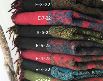 May include: A stack of eight colorful scarves with paisley patterns. The scarves are folded and stacked on top of each other. The top scarf is black with a red and green paisley pattern. The second scarf is red with a black and blue paisley pattern. The third scarf is black with a green and gold paisley pattern. The fourth scarf is red with a black and blue paisley pattern. The fifth scarf is black with a green and gold paisley pattern. The sixth scarf is green with a black and blue paisley pattern. The seventh scarf is red with a black and gold paisley pattern. The eighth scarf is black with a red and green paisley pattern. Each scarf has a label with the text "E-1-22", "E-2-22", "E-3-22", "E-4-22", "E-5-22", "E-6-22", "E-7-22", and "E-8-22".