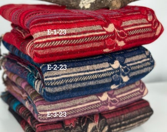 Peut inclure: Une pile de quatre couvertures tissées de couleurs et de motifs différents. La couverture du dessus est rouge avec un motif blanc et bleu. La deuxième couverture est bleue avec un motif blanc et marron. La troisième couverture est violette avec un motif blanc et marron. La couverture du bas est noire avec un motif blanc et marron. Les couvertures sont étiquetées avec le texte "E-1-23", "E-2-23", "E-3-23", et "E-4-23".