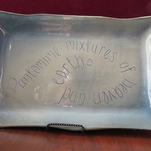 May include: A rectangular ceramic serving platter with a light blue glaze. The platter has a slightly irregular shape and features the handwritten text "Pantomime earth mixtures of heaven and".