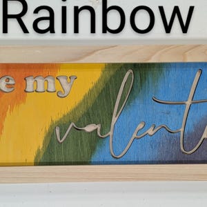 Handmade cypress frame with Baltic birch rainbow background. The natural Baltic birch letters read ...be my Valentine. Be my is in printed letters and the valentine in script. The words are recessed into the wood.