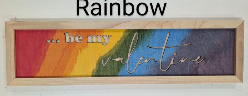 Handmade cypress frame with Baltic birch rainbow background. The natural Baltic birch letters read ...be my Valentine. Be my is in printed letters and the valentine in script. The words are recessed into the wood.
