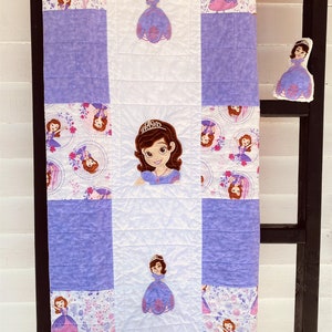 May include: A purple and white patchwork quilt with a princess character design. The quilt features a variety of scenes with the princess in different poses and settings. The quilt is made of soft, comfortable fabric and is perfect for cuddling up on the couch or in bed.