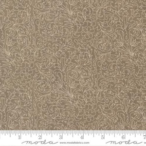 May include: Tan fabric with a repeating floral and leaf pattern in a lighter beige color. The design features swirling lines and small flower shapes. A ruler is at the bottom, with measurements in inches.