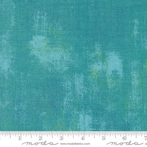 May include: Teal blue fabric with a subtle distressed texture and a light green and blue mottled pattern. The fabric is shown with a ruler for scale.