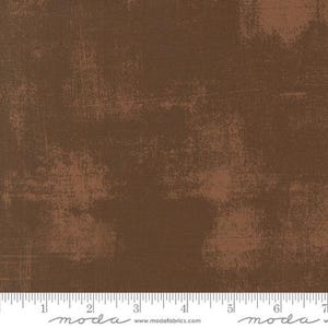 May include: Brown fabric with a distressed, textured appearance. The fabric has a mottled effect with lighter brown patches and a subtle linear pattern. The overall look is rustic and aged, suitable for various craft projects.