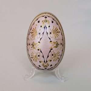 May include: A pink Easter egg with a delicate gold and black floral design. The egg is on a clear plastic stand.