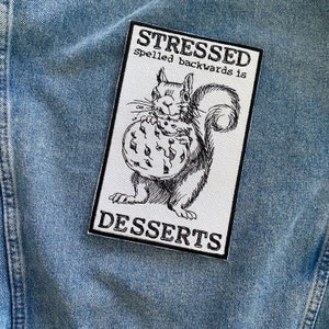 May include: A white patch with black text and a black and white illustration of a squirrel holding a cookie. The text reads "Stressed spelled backwards is Desserts."