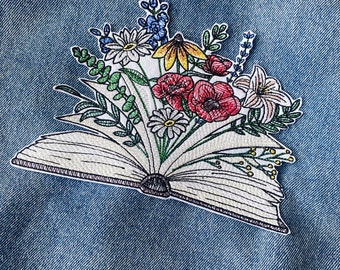 Peut inclure: Un patch brodé représentant un livre ouvert avec un bouquet de fleurs colorées qui en sortent. Les fleurs sont rouges, jaunes, blanches, bleues et vertes.