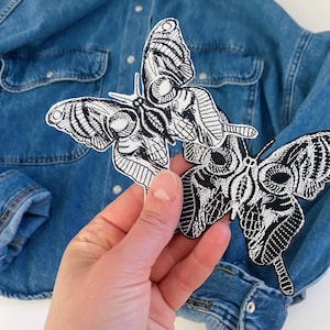 Op de afbeelding: Twee geborduurde vlinderpatches in zwart en wit. De vlinders hebben ingewikkelde details en een schedel-achtig ontwerp.