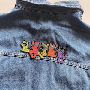 May include: Five embroidered iron-on patches of cats wearing sunglasses. The cats are in a row, facing right. The cats are yellow, red, yellow, orange, and purple.