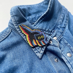 May include: A denim shirt with a black and rainbow embroidered cat patch on the collar.