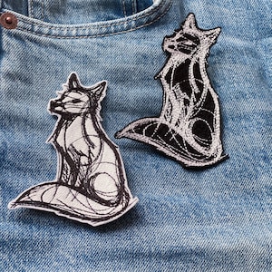 Könnte beinhalten: Zwei gestickte Fuchsflicken in Schwarzweiß auf einem blauen Jeansstoff.