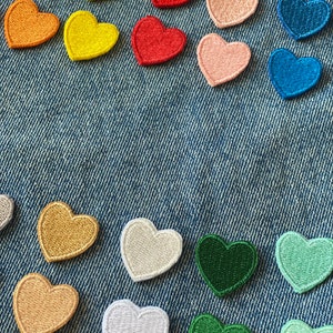 May include: Assortment of colorful felt heart patches in various shades of red, orange, yellow, green, blue, and pink. The patches are arranged on a blue denim background.