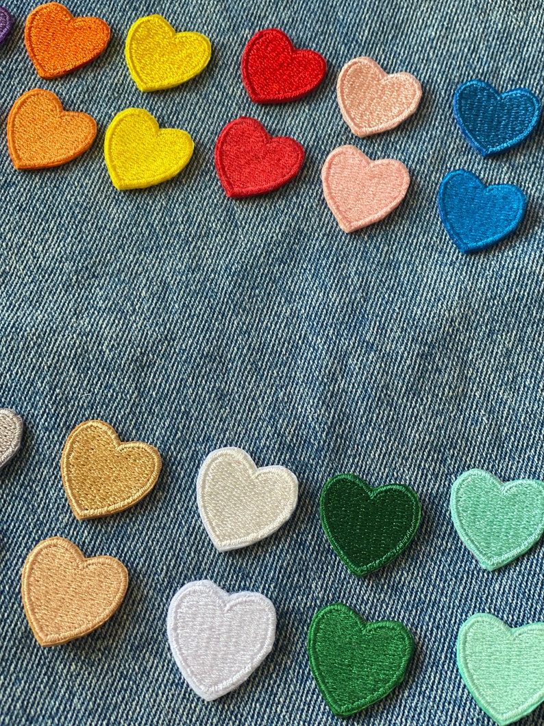 May include: Assortment of colorful felt heart patches in various shades of red, orange, yellow, green, blue, and pink. The patches are arranged on a blue denim background.