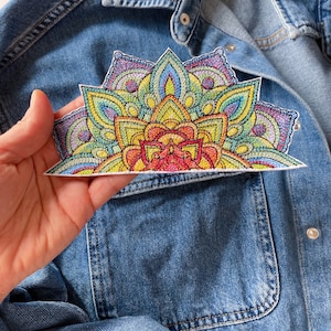 May include: A colorful embroidered patch in the shape of a half-circle mandala. The patch features a variety of colors, including red, orange, yellow, green, blue, and purple. The patch is perfect for adding a touch of bohemian style to clothing, bags, or other accessories.