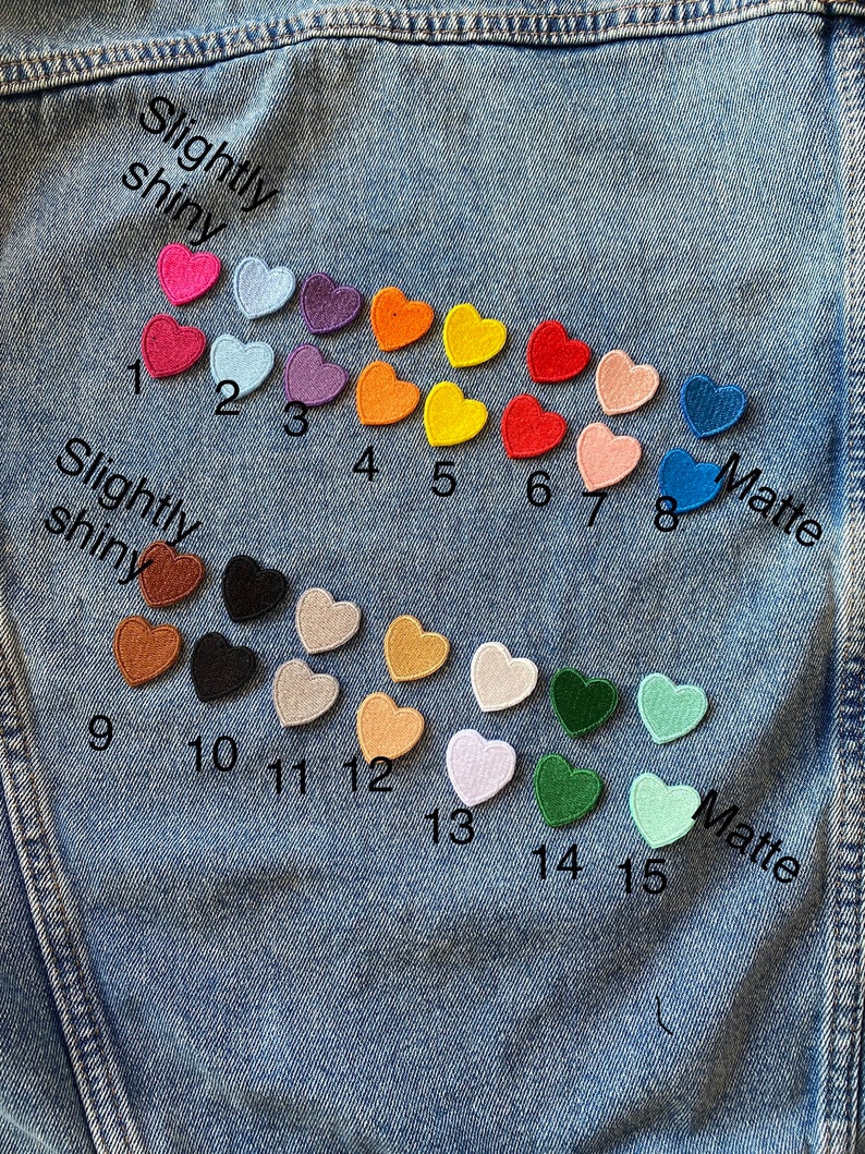 May include: Fifteen felt heart patches in various colors, including red, pink, orange, yellow, green, blue, and brown. The patches are arranged in two rows on a blue denim background. The top row is labeled "Slightly shiny" and the bottom row is labeled "Matte".