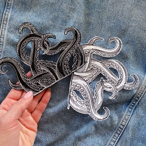 May include: Two iron-on patches featuring an octopus design. One patch is black and white, and the other is white with black outlines.