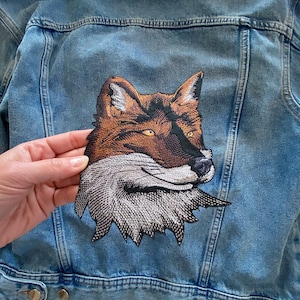 May include: A blue denim jacket with a brown, black, and white embroidered fox head patch on the back.
