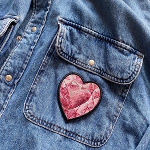 Peut inclure: Une veste en jean avec un patch en forme de cœur rose cousu sur la poche.