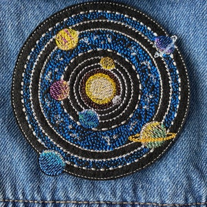May include: Embroidered patch depicting a black and blue solar system with a yellow sun and multiple planets in orbit. The patch is circular and has a white outline.